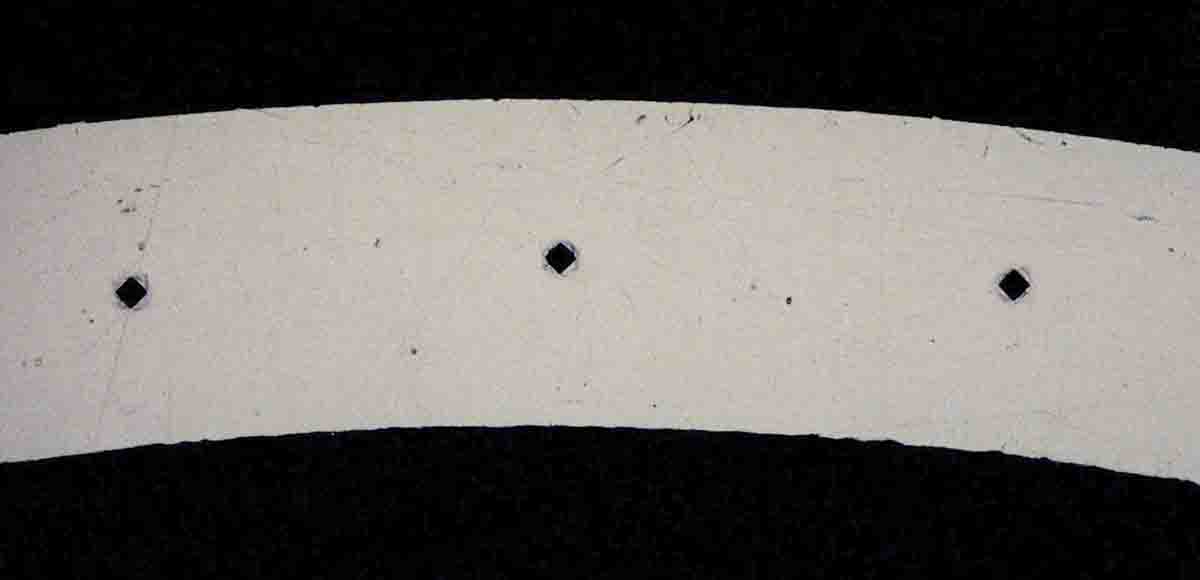 This cross section of a case neck is magnified ­­­­100 times and shows where three test samples were taken as indicated by outlines of indents by the pyramid-shaped penetrator. The voids are darkened in shadow from the side light. The widths of these indents are measured under a microscope.